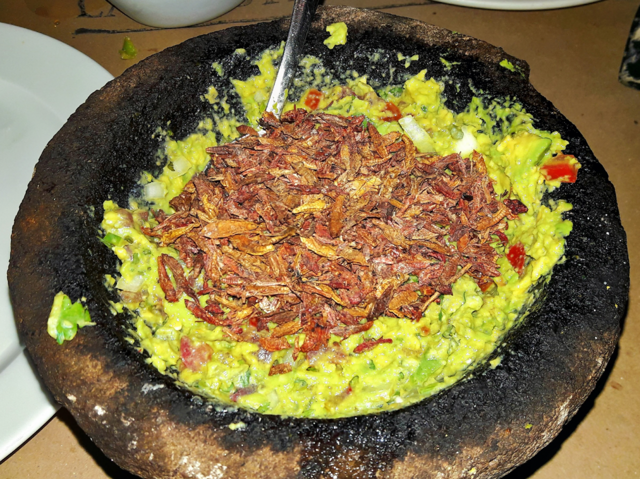 Chunky green guacamole in a stone molcajete with lime wedges